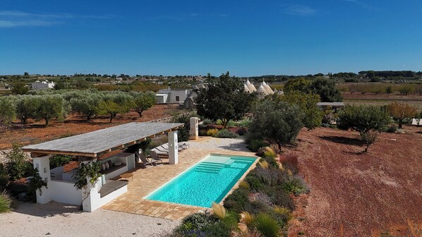 Piscina com pérgola, um pequeno edifício e oliveiras ao fundo.