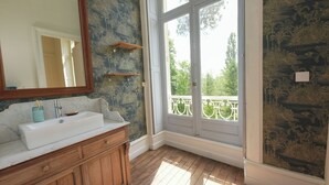 A bathroom with a marble sink, wooden cabinets, a large mirror, and a view of a balcony with a railing. - The Château and its Orangery (Langeais)
