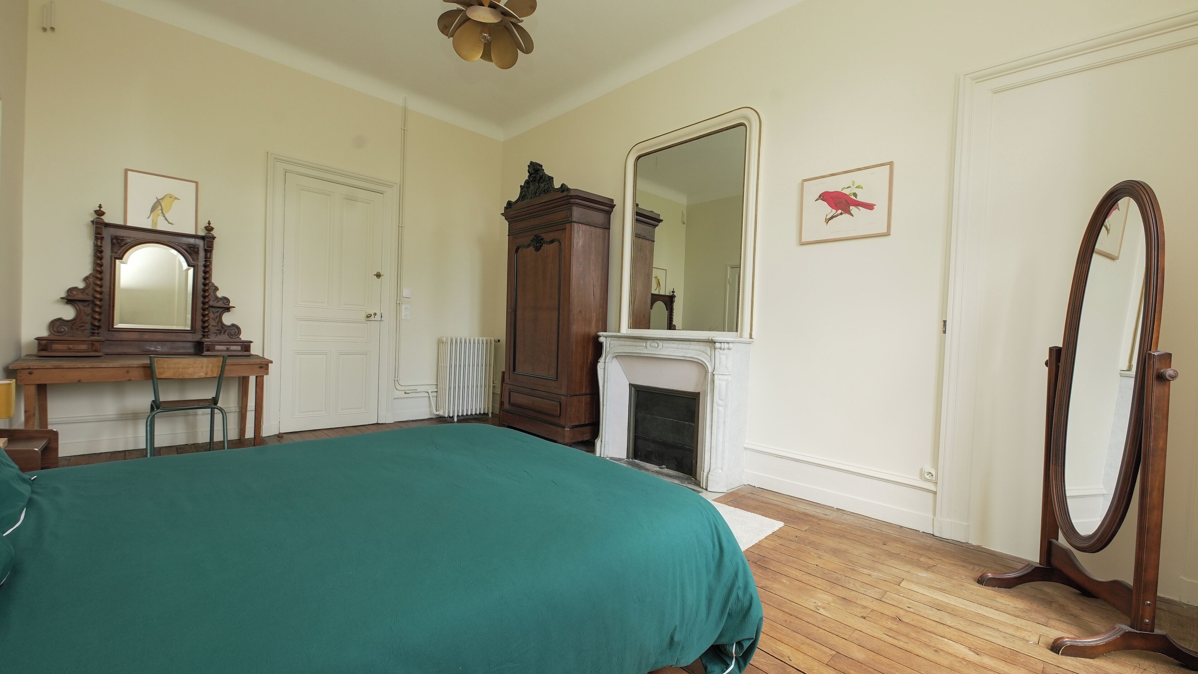A bedroom with a bed, dresser, mirror, and fireplace.