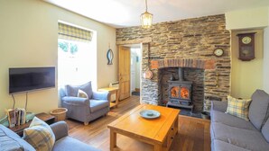 A cozy living room with a stone fireplace, a flat-screen TV, and comfortable seating. - Bywell, Llangrannog - Three Bedroom Cottage, Sleeps 6 (Llangrannog)