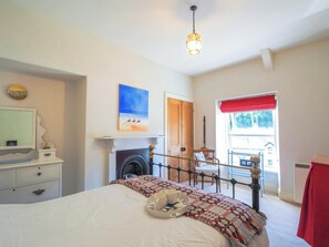 A bedroom with a bed, a fireplace, a television, and a window with a red valance.