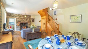 A dining area with a round table set for six, a fireplace, and a staircase leading to another level. - Bywell, Llangrannog - Three Bedroom Cottage, Sleeps 6 (Llangrannog)
