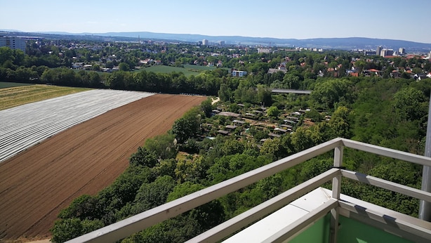 A view from a balcony overlooking a cityscape with fields and residential areas.