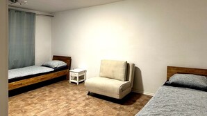 A small, well-lit room with two beds, a chair, and a small table.