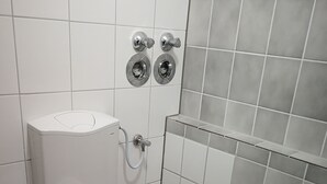 A small, clean bathroom with a white toilet, a wall-mounted bidet, and a shower area.