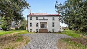 Une maison à deux étages avec un toit rouge et une véranda à l’avant.