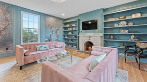 Un salon avec deux canapés roses, une cheminée et un téléviseur fixé au mur.