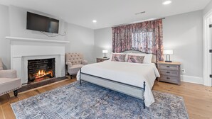 Une chambre à coucher avec une cheminée, un lit, un téléviseur fixé au-dessus de la cheminée et une table de chevet avec une lampe.