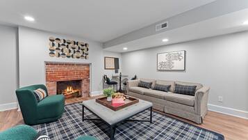 Una sala moderna con chimenea de ladrillo, un sillón verde, un sofá gris y un tapete escocés.