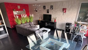 Ein modernes Wohnzimmer mit einem Esstisch mit Glasplatte, einem grauen Sofa und einem Flachbildfernseher.
