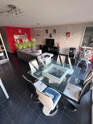 Una sala de estar moderna con una mesa de comedor de vidrio, un sofá gris y un televisor de pantalla plana.