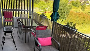 Ein Balkon mit Gartenmöbeln, Blick auf eine grüne Landschaft und ein Holzzaun.
