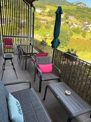 Un balcon avec des meubles d’extérieur, une vue sur un paysage verdoyant et une clôture en bois.