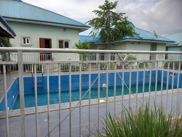 A rectangular swimming pool with a white fence in the foreground. - Grovehill Hotel Plus Ilesa  (Ilesa)
