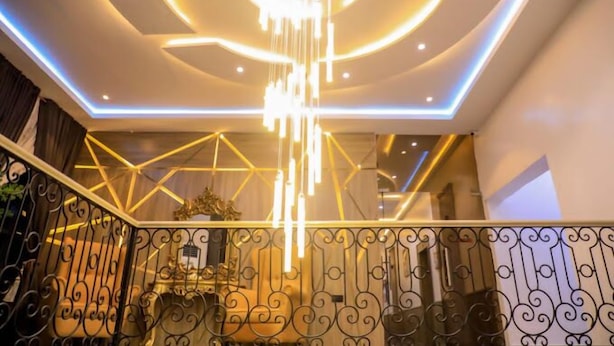 A modern interior with a geometric light fixture and a staircase with ornate railings. - Grovehill Hotel Plus Ilesa  (Ilesa)