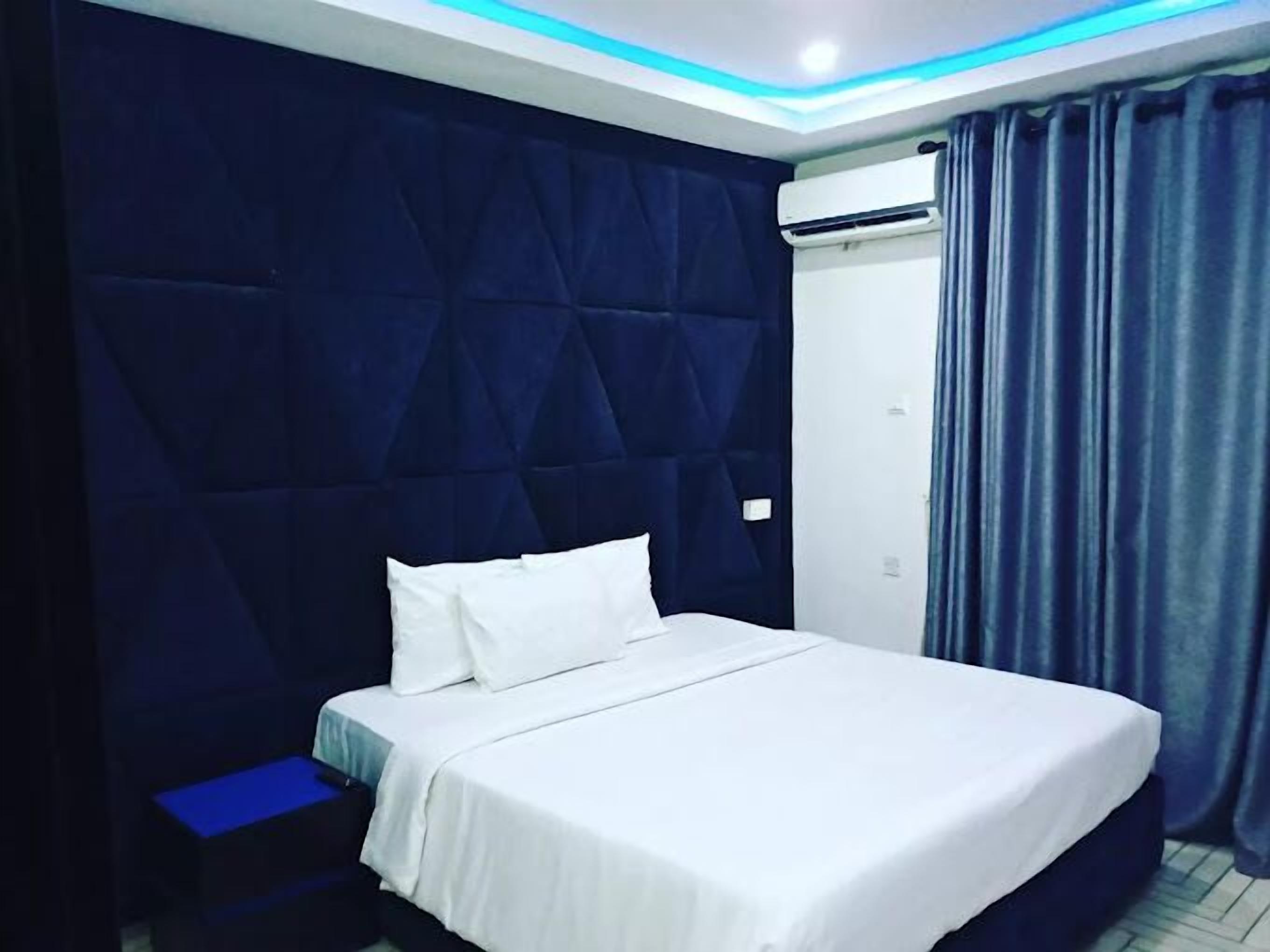 A hotel room with a large bed, a small bedside table, a headboard, and an air conditioning unit.