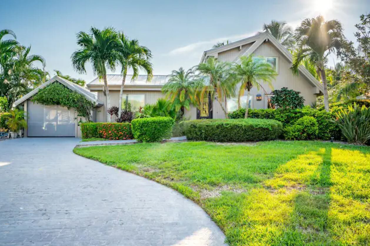 A residential property with a paved driveway, a well-maintained lawn, and a variety of tropical plants.