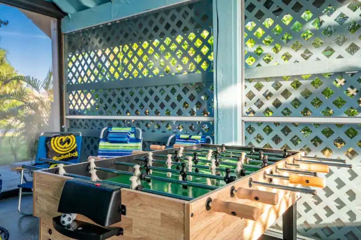 A foosball table in a room with a lattice window and a pool table in the background.