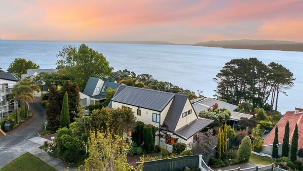 A residential area with houses, a clear view of the sea, and a sunset sky.
