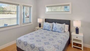 A bedroom with a bed, two bedside tables, and two windows.
