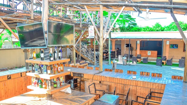 An outdoor bar area with wooden furniture and a bar counter displaying various bottles. - K27 Premier Backpackers (Dar es Salaam)