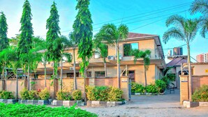 A multi-story building with a flat roof, surrounded by greenery and palm trees. - K27 Premier Backpackers (Dar es Salaam)