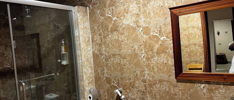 Une salle de bain avec une douche à parois de verre, un lavabo et un mur en marbre.