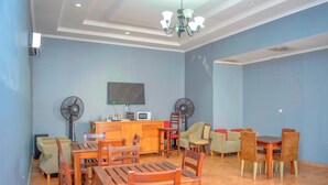 A dining area with wooden tables and chairs, a television, and two wall fans. - K27 Premier Backpackers (Dar es Salaam)