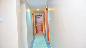 A narrow hallway with a wooden door at the end, light-colored walls, and a tiled floor. - K27 Premier Backpackers (Dar es Salaam)