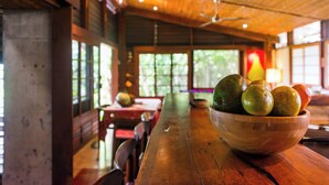 A wooden dining table with a bowl of fruit in the center, surrounded by chairs. - Jungle Villa with ocean view, shared infinity pool, wildlife, open-air living. (San Juan del Sur)
