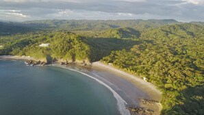 An aerial view of a coastal area with a beach, dense forest, and hills in the background. - Jungle Villa with ocean view, shared infinity pool, wildlife, open-air living. (San Juan del Sur)
