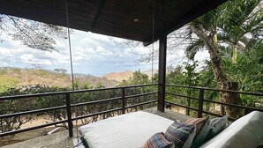 A balcony with a bed, a view of a mountainous landscape, and a palm tree. - Jungle Villa with ocean view, shared infinity pool, wildlife, open-air living. (San Juan del Sur)