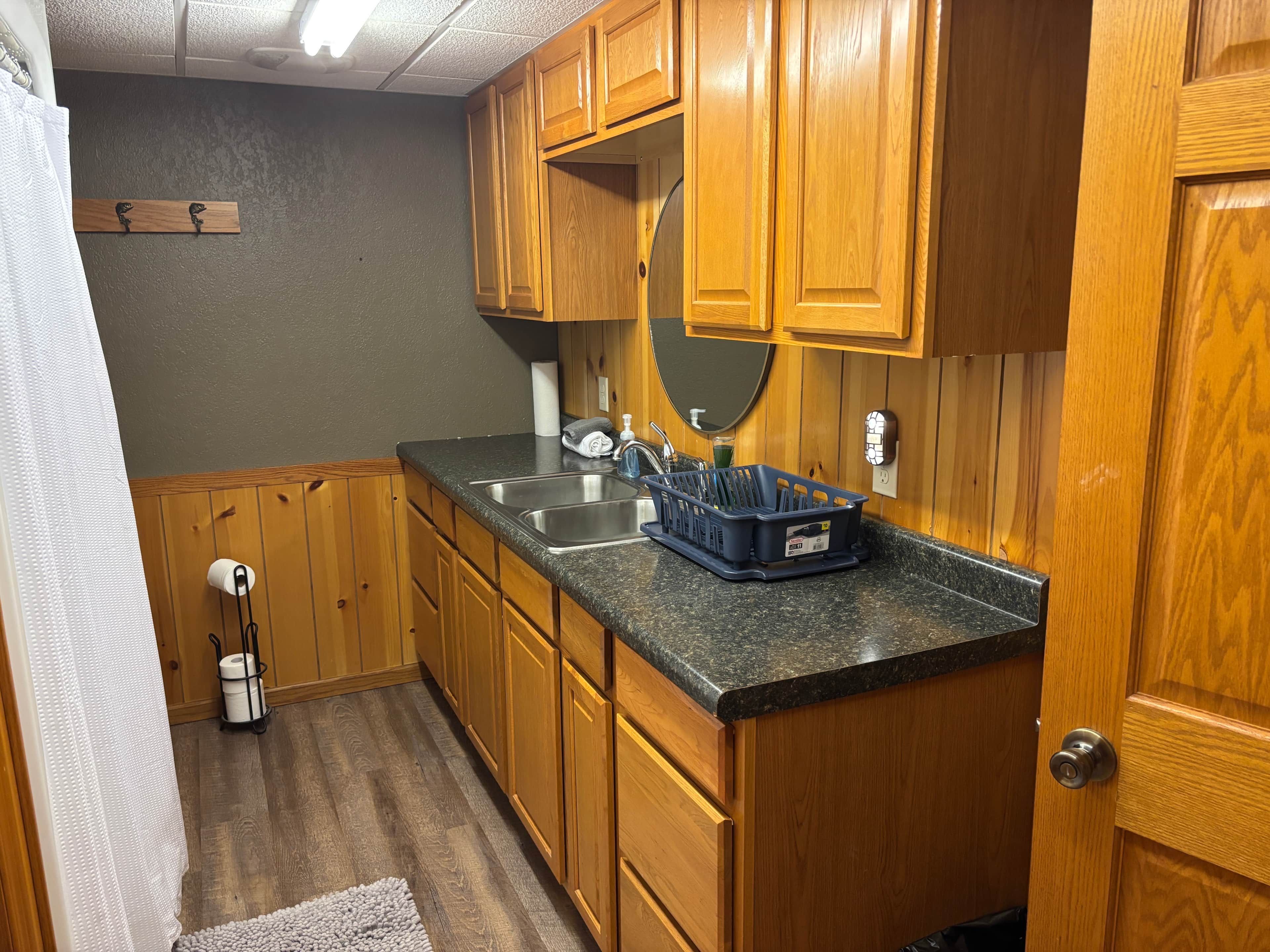 Una cocina con armarios de madera, encimera de granito, un lavabo y un escurreplatos.