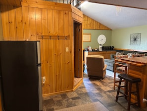 A kitchen with wooden cabinets, a refrigerator, a clock, and a microwave.