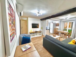 A living room with a sofa, a dining table, and a TV mounted on the wall.