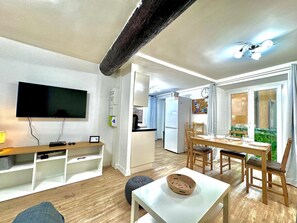 Ein modernes Wohnzimmer mit Flachbildfernseher, Holzmöbeln und einem Essbereich mit Tisch und Stühlen.