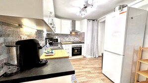 A modern kitchen with a black countertop, white cabinets, a stainless steel range hood, and a white refrigerator. - Angle droite (Nice)