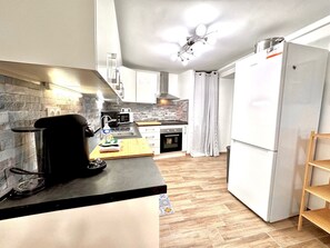 A modern kitchen with a black countertop, white cabinets, a stainless steel range hood, and a white refrigerator.
