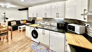A modern kitchen with white cabinets, a built-in washing machine, a dishwasher, a microwave, and a wooden dining table with chairs. - Angle droite (Nice)