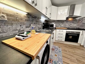 A modern kitchen with a stone backsplash, stainless steel appliances, and a wooden countertop.