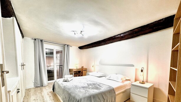 A bedroom with a bed, bedside table, lamp, and a view of a balcony. - Angle droite (Nice)