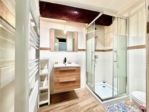 Ein modernes Badezimmer mit einer Duschkabine aus Glas, einem Holzausziehtisch und einem weißen Waschbecken.