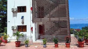 Un immeuble de deux étages avec une façade blanche, des unités de climatisation et un balcon agrémenté de plantes en pot.