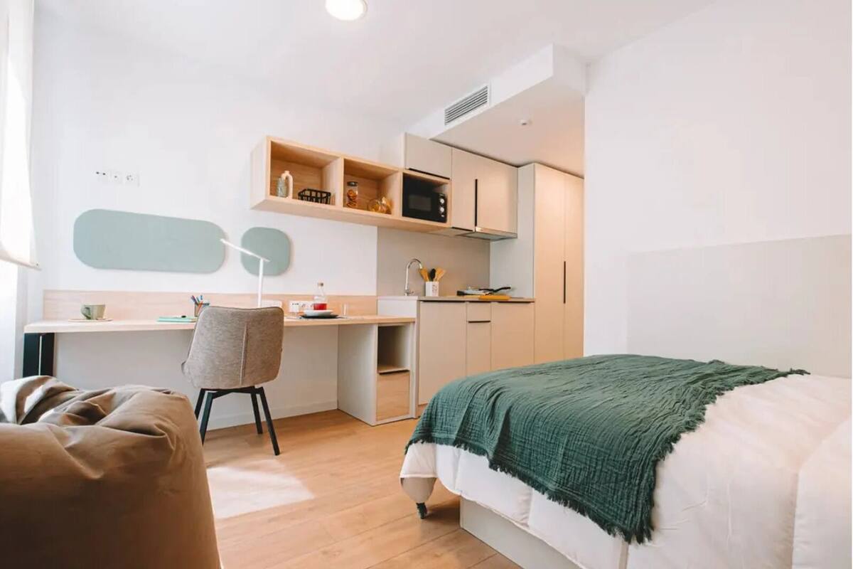 A modern, compact bedroom with a bed, a desk, and a chair.