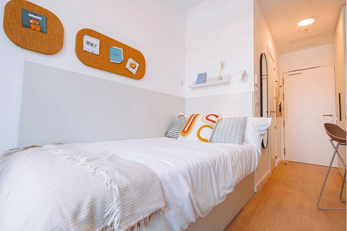 A bedroom with a bed, a wall-mounted corkboard, and a door.