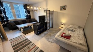 Une chambre d’hôtel moderne équipée d’un canapé, d’une petite table, d’une télévision, d’un lit et offrant une vue sur les arbres par la fenêtre.
