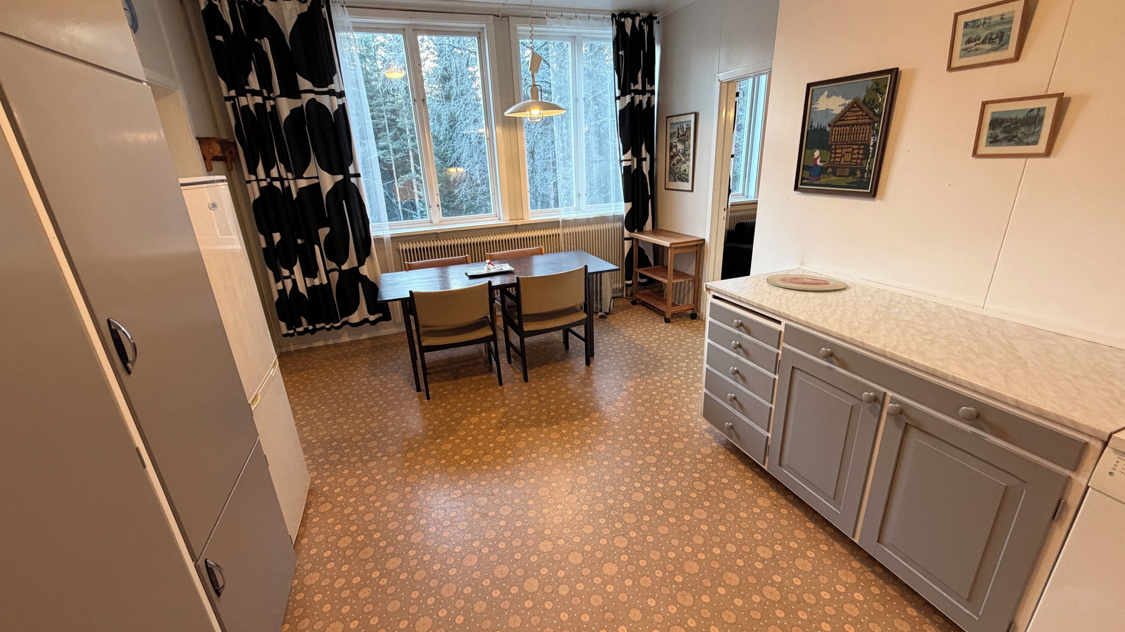 A kitchen with a dining table, chairs, a refrigerator, a radiator, and a cabinet.