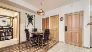 A dining area with a wooden table and chairs, a hanging light fixture, and a bookshelf.