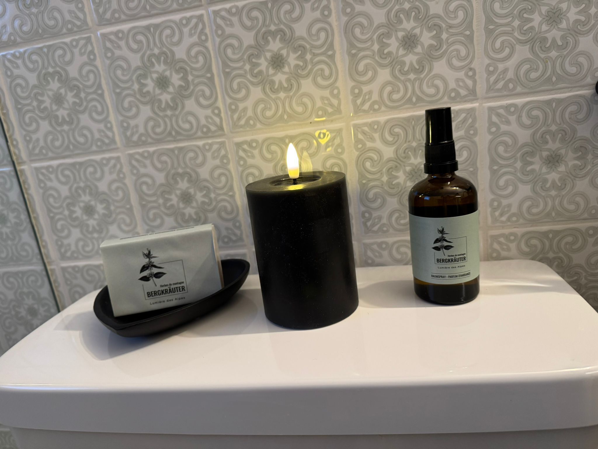 A bathroom with a white toilet, a black candle, and a bottle of Bergkrauter essential oil.