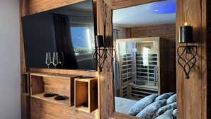 A wooden-framed TV with a landscape view, two candles, and a mirror reflecting a wardrobe and bed. - Bergbijou - Luxurious vacation home with sauna, whirlpool, infrared and mountain views (Scuol)